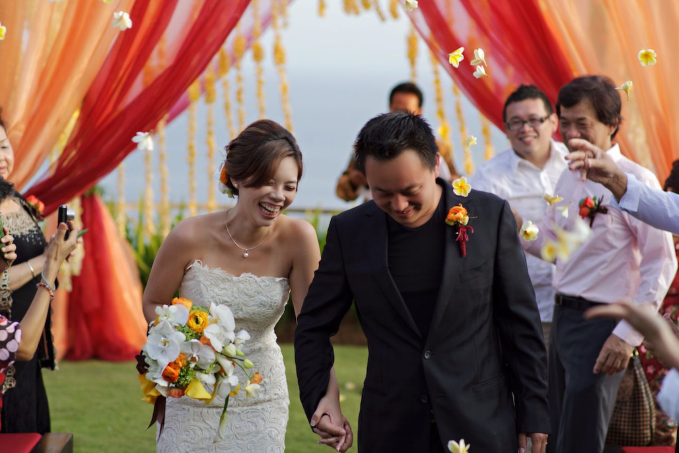 couple walking down aisle as guest showering them with frangipani